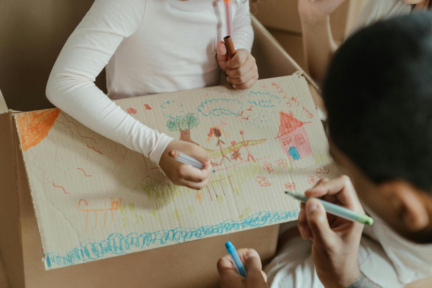 Kind tekent huizen op een verhuisdoos met haar vader om huizen en wonen te begrijpen