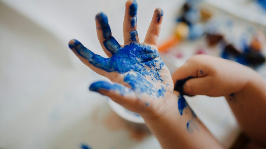 Kinderhand met blauwe verf toont creativiteit tijdens schilderactiviteit in de klas of thuis